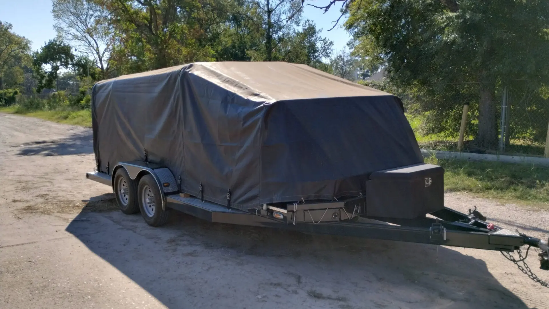 Covered utility trailer parked outdoors on a sunny day.