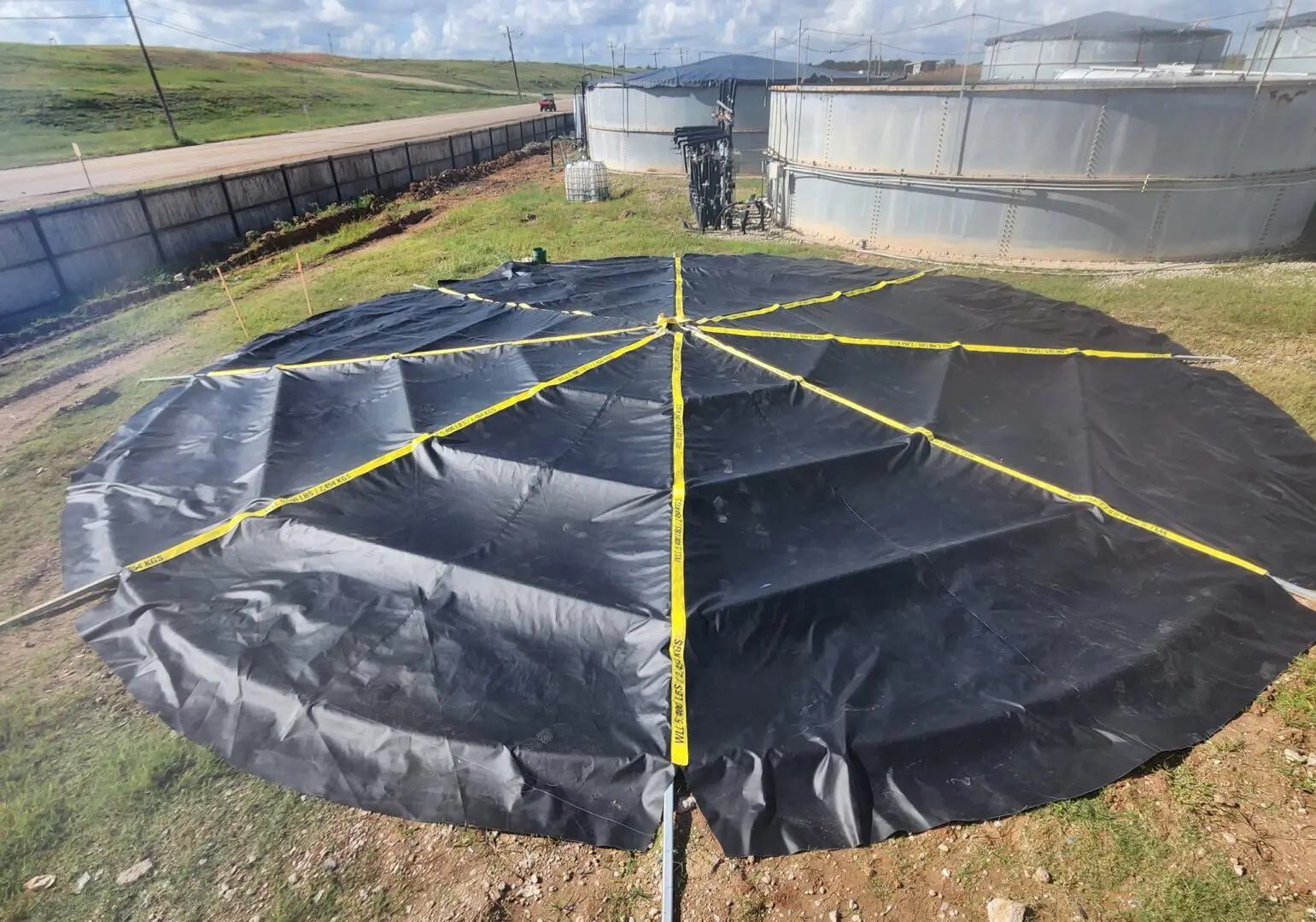Large industrial circular tank covered with black tarp and yellow tape.