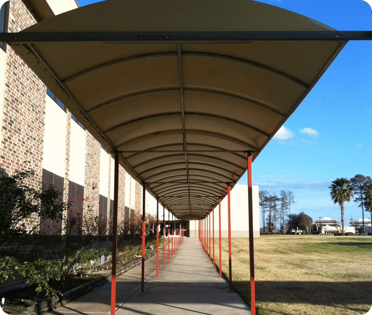 Covered walkway with red poles and trees.