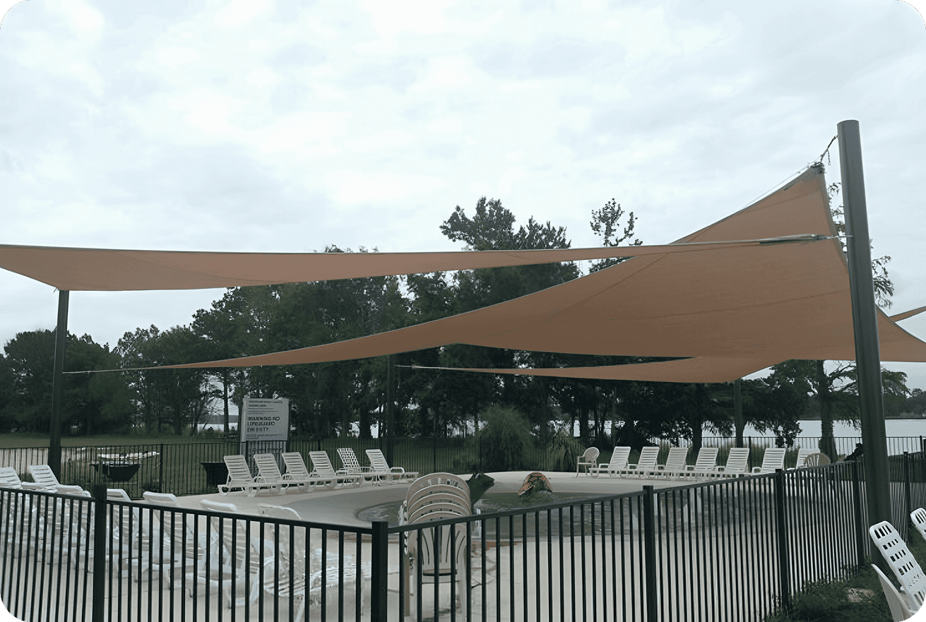 Empty pool area with sun shades and lounge chairs on a cloudy day.