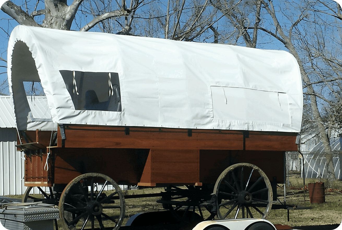 A covered wooden wagon with spoked wheels under a clear sky.